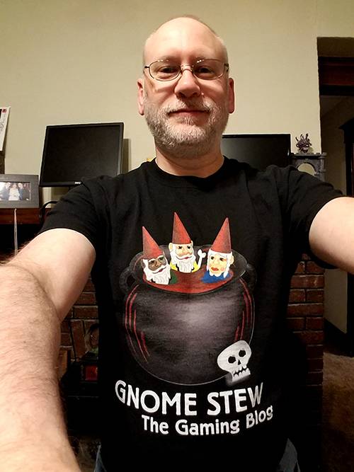 Selfie shot of a m an with glasses and the Gnome Stew logo shirt in black on his chest.