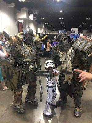 A child in star wards stormtrooper cosplay has two adult guardians in impressive armor cosplay next to them. 