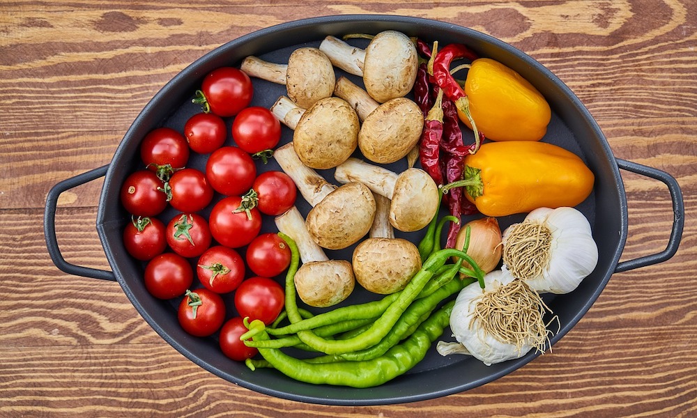 A stew pot with an array of vegetables: tomatos, green beans, mushrooms, garlic, and peppers