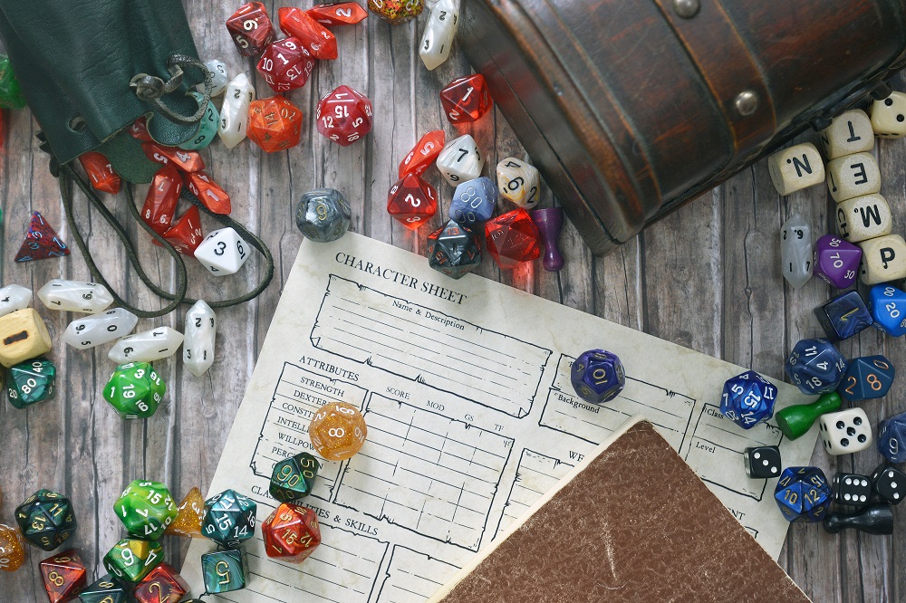 Tabletop roleplaying flat lay with colorful RPG and game dices, character sheet, rule book and treasure chest on wooden desk