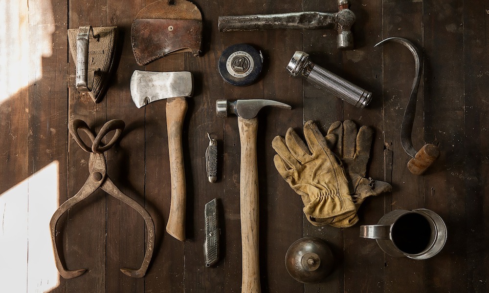A series of tools on a wood surface: gloves, hammer, axe, flashlight, pliers etc.