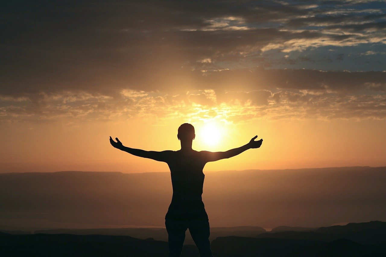 A person standing before the rising sun with their arms open to the day.