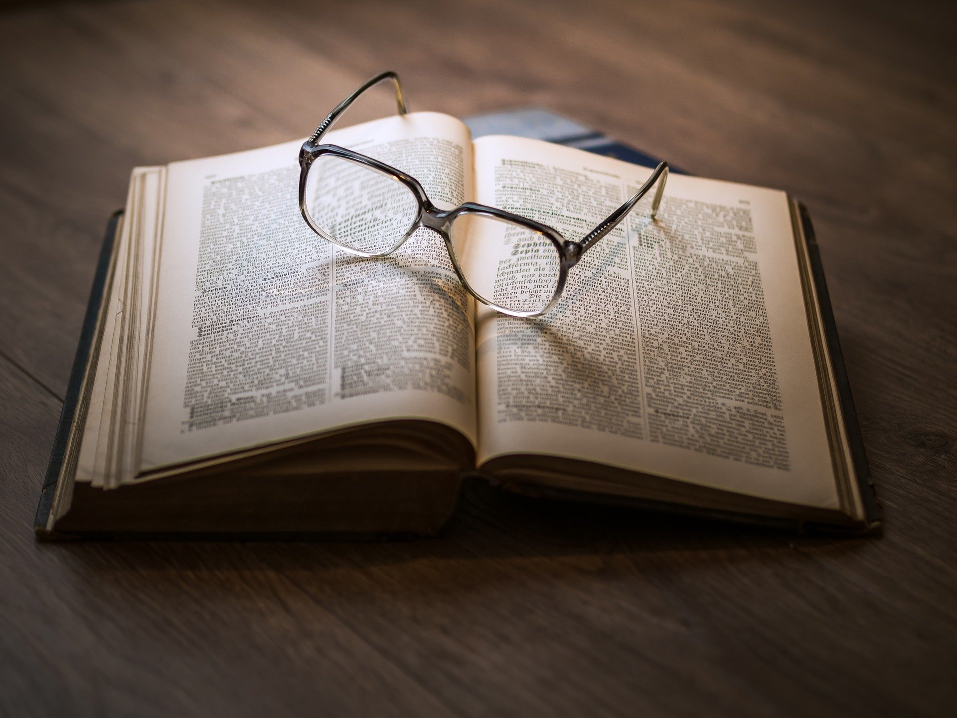 An open book on a desk, with a pair of glasses resting on the pages.
