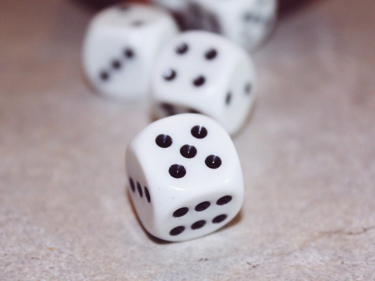 Several dice rolling across a surface, a die with the number five is in foreground.