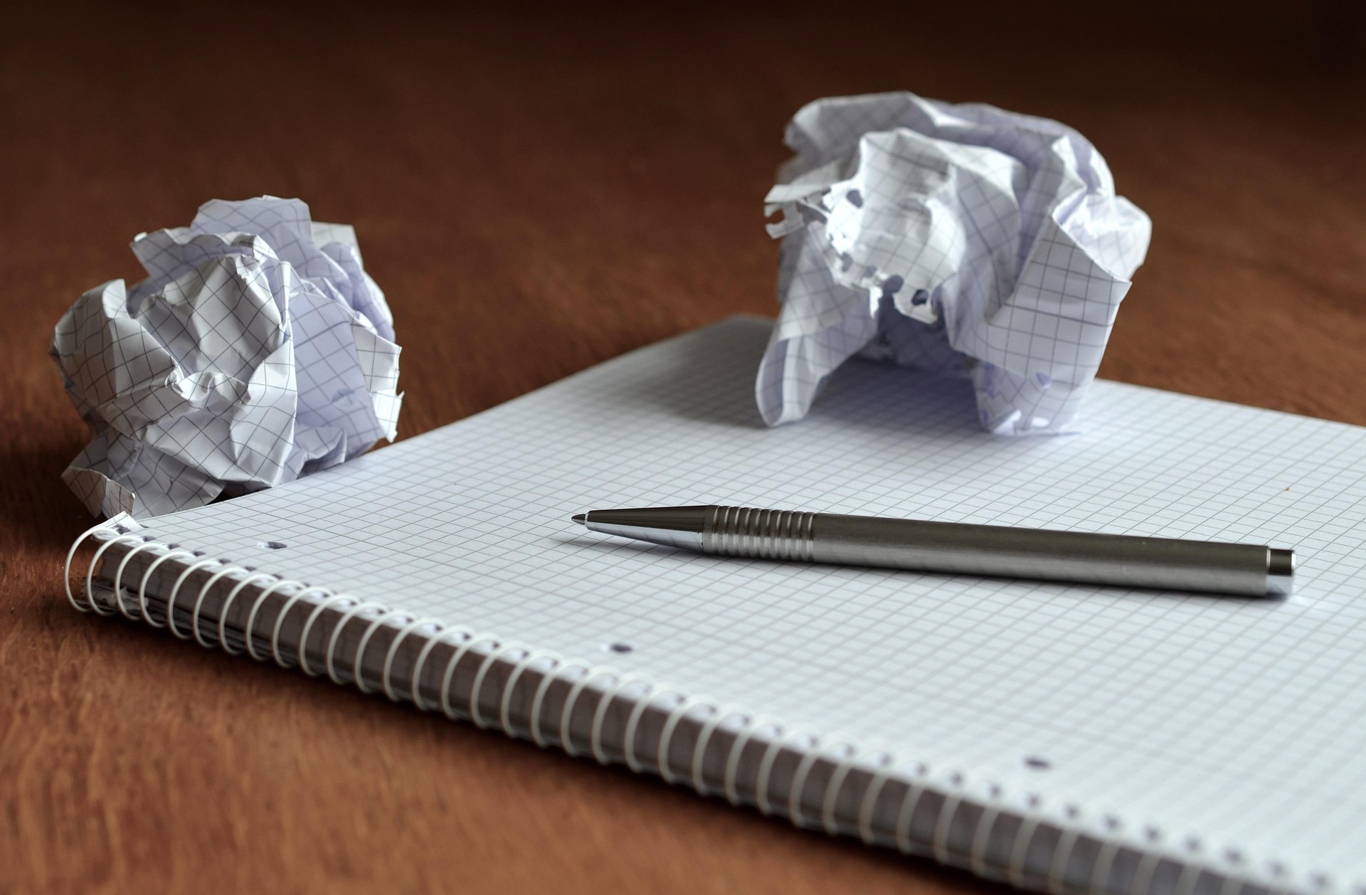 A blank notepad and pen on a desk, with two crumpled up sheets of a paper from the notebook.